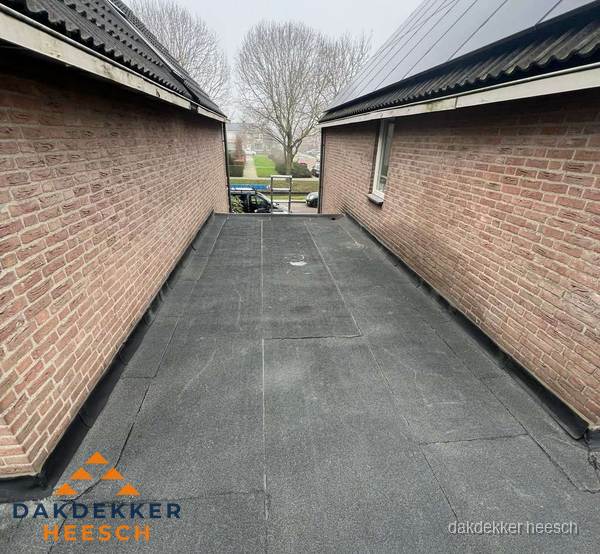 Plat dak met bitumen dakbedekking tussen bakstenen muren in Heesch